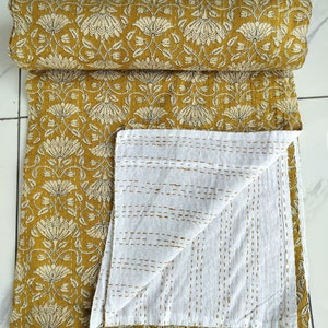 May include: A mustard yellow kantha quilt with a white floral pattern. The quilt is folded in half, revealing the white cotton underside with a subtle stitching pattern.