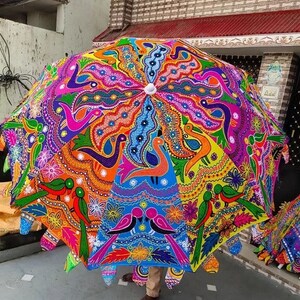 Puede incluir: Un gran paraguas colorido con un dise&ntilde;o pintado a mano. El paraguas presenta un caleidoscopio de colores, incluyendo rosa, naranja, azul y verde, con patrones intrincados y motivos de aves. El paraguas est&aacute; abierto, mostrando su forma circular completa.