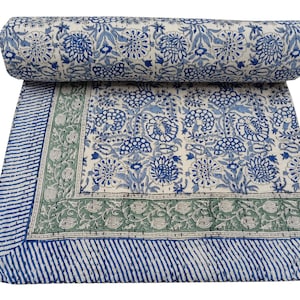 May include: A rolled-up, floral-patterned quilt with a cream background and blue floral designs. The quilt has a blue and green border with a striped edge. The design features a repeating pattern of flowers and leaves.