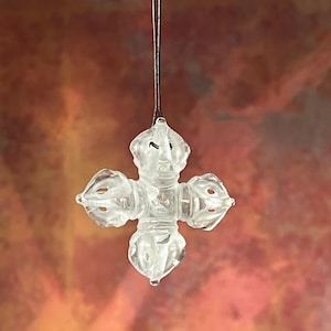 May include: A clear crystal prayer wheel pendant with a detailed design. The pendant is hanging from a thin cord.