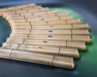 May include: A set of wooden xylophone bars with clear acrylic tubes. The bars are arranged in a semi-circle and have different colored labels.