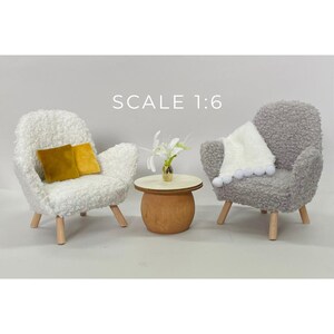 May include: Miniature furniture set featuring two armchairs, a small round table, and decorative accents. One armchair is white, the other is gray. The table is wood-toned with a gold vase and white flowers. The text "SCALE 1:6" is visible.