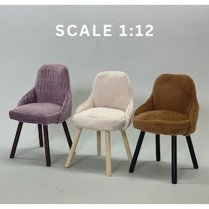 Puede incluir: Tres sillas en miniatura de diferentes colores: morado, blanco y marrón. Las sillas están hechas de madera y tienen una tapicería de tela suave. Las sillas son todas del mismo estilo, con un respaldo redondeado y cuatro patas. Las sillas están dispuestas en fila, con la silla morada a la izquierda, la silla blanca en el centro y la silla marrón a la derecha. Las sillas están todas a escala 1:12.
