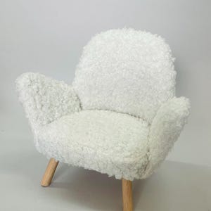 May include: A small, white, fluffy armchair with a rounded back and armrests. The chair has a soft, textured appearance and is supported by four wooden legs.