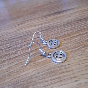 May include: A pair of silver button earrings with a simple design. Each earring features a round button with four holes.
