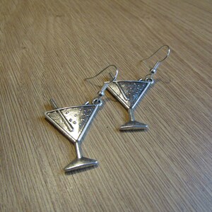 May include: A pair of silver earrings shaped like martini glasses with a straw detail.