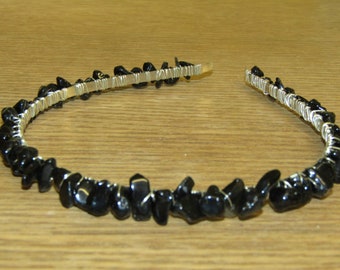Puede incluir: Una diadema delicada hecha de alambre plateado envuelto alrededor de piedras preciosas negras.