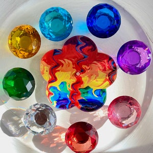 May include: A collection of colorful, faceted glass gems and a flower-shaped charm. The gems are in various colors, including yellow, blue, green, purple, pink, and red. The charm has a rainbow swirl design and the text "Stamptabulous".