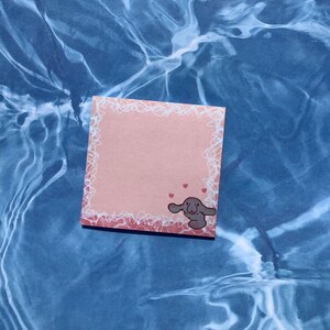 May include: A pink sticky note with a white lace border and a cartoon illustration of a manatee with hearts. The note says "peachicream" at the bottom.