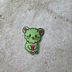 May include: Green fuzzy bear sticker with pink watermelon slices on its ears and holding a pink watermelon slice.