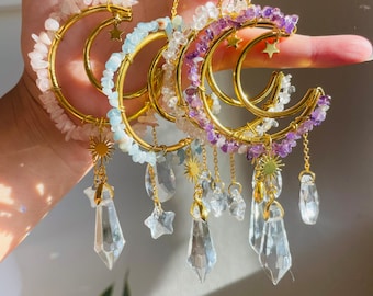 May include: Three gold crescent moon necklaces with crystal accents. Each necklace features a different colour of semi-precious stones: pink, light blue, and purple. The necklaces have crystal teardrop and star charms.