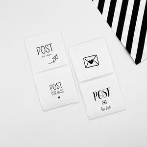 Könnte beinhalten: Vier weiße Aufkleber mit dem Wort "POST" und "für dich" in Handschrift. Jeder Aufkleber hat eine andere schwarze Grafik: ein Papierflugzeug, einen Umschlag, ein Herz und einen kleinen Umschlag. Im Hintergrund befindet sich eine schwarz-weiß gestreifte Tasche.
