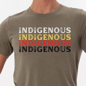 May include: A green t-shirt with the word "INDIGENOUS" repeated four times in a stacked design. The word is in white, yellow, red, and black.