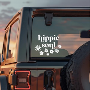 May include: White vinyl decal with the words "hippie soul" in a decorative font, accompanied by floral designs. The decal is affixed to the rear window of a black vehicle, with a sunset visible in the background.