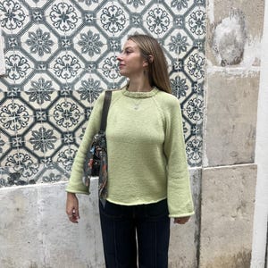 Puede incluir: Un suéter de punto de manga larga en color verde lima con cuello redondo acanalado y mangas ligeramente acampanadas. El suéter presenta un patrón de punto jersey en toda la prenda, lo que proporciona una textura suave y uniforme.
