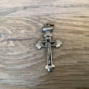 Puede incluir: Un colgante de cruz de plata con fondo negro y una figura de Jesucristo de plata. El colgante tiene un bucle en la parte superior para sujetarlo a una cadena.