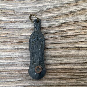 Op de afbeelding: Een klein, grijs metalen hanger met een gedetailleerd beeld van de Maagd Maria. De hanger heeft een lus aan de bovenkant om aan een ketting of koord te bevestigen.