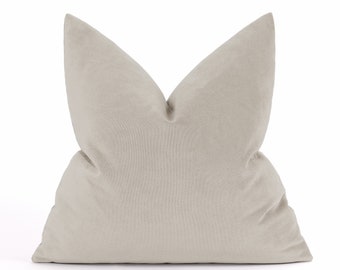 May include: A light beige throw pillow with a soft, velvety texture. The pillow is rectangular and has a pointed shape at the top.