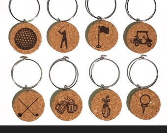 May include: Set of eight golf-themed wine charms. Each charm features a cork disc with a silver-colored ring. The cork discs have various golf-related designs, including a golf ball, golfer, flag, golf cart, crossed clubs, beer mugs, golf bag, and golf tee.