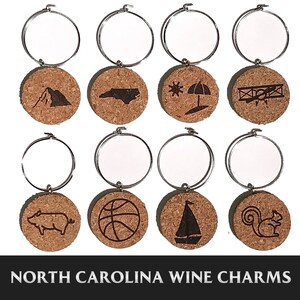 May include: Set of eight North Carolina wine charms featuring various state-themed designs, including a mountain, a pig, a basketball, a sailboat, a squirrel, a state outline, a beach umbrella, and an airplane. Each charm is made of cork and has a silver metal ring.