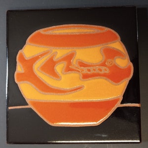 May include: Square ceramic tile with a black background and a stylized orange and yellow pot design. The pot features a decorative pattern and is outlined with a metallic gold color. The tile has a glossy finish.