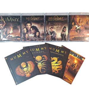 May include: A collection of DVDs and Blu-rays from "The Mummy" film franchise. The covers feature images of actors and movie titles in gold and white against dark backgrounds. The titles include "The Mummy", "The Mummy Returns", "Tomb of the Dragon Emperor", and "The Scorpion King".
