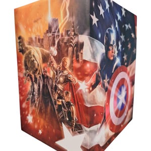 K&ouml;nnte beinhalten: W&uuml;rfelf&ouml;rmige Box mit einer Collage von Marvel-Superhelden. Die Illustration zeigt Captain America, Thor und Hulk. Der Hintergrund zeigt eine amerikanische Flagge und eine Stadtlandschaft mit Blitzen.