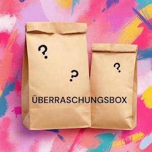 Op de afbeelding: Twee bruine papieren zakken met vraagtekens erop. De grotere zak heeft de tekst "ÜBERRASCHUNGSBOX" erop gedrukt.