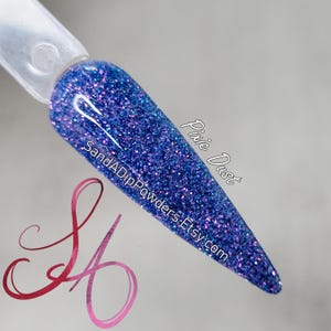 Puede incluir: Primer plano de un esmalte de uñas azul con purpurina y acabado holográfico. El esmalte se llama "Pixie Dust" y es de la marca "SandADipPowders.Etsy.com".