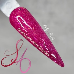 May include: A close-up of a pink nail polish with gold glitter. The polish is called "Ruby Flakie" and is from SandADipPowders.Etsy.com.