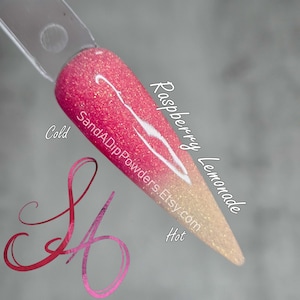 May include: A close-up of a nail with a pink to yellow ombre dip powder design. The nail is labeled "Raspberry Lemonade" and "SandADipPowders.Etsy.com". The words "Cold" and "Hot" are written on either side of the nail.