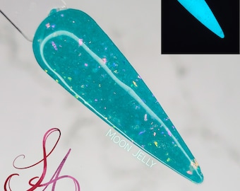 May include: A teal nail swatch with iridescent glitter and the text "MOON JELLY". A smaller inset image shows the swatch glowing bright blue. The swatch is on a clear stick. The letters "SA" are in a cursive font.