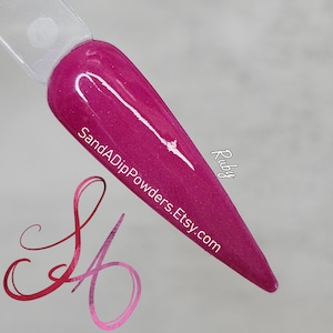 Puede incluir: Primer plano de un esmalte de uñas rosa oscuro con acabado brillante. El esmalte está en una punta de uña y el texto "SandADipPowders.Etsy.com" y "Ruby" son visibles.