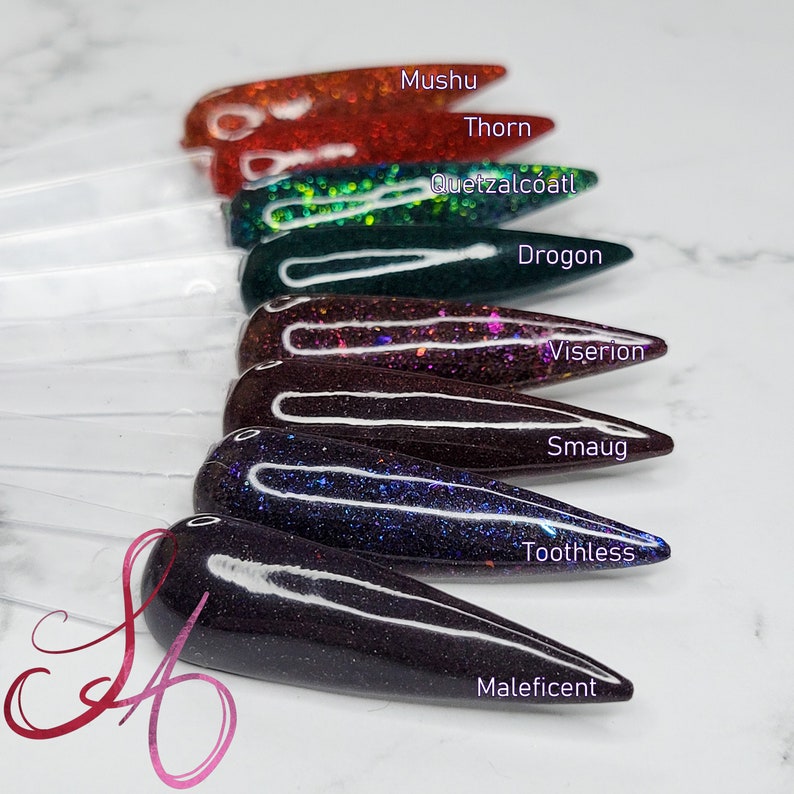 K&ouml;nnte beinhalten: Acht verschiedene Farben von Glitzer-Nagellack in einer Reihe, beschriftet mit den Namen Mushu, Thorn, Quetzalcoatl, Drogon, Viserion, Smaug, Toothless und Maleficent.