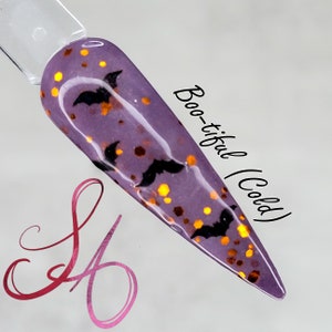 May include: A purple nail polish with a glittery finish and black bat silhouettes. The text "Boo-tiful (Cold)" is written on the right side of the image.