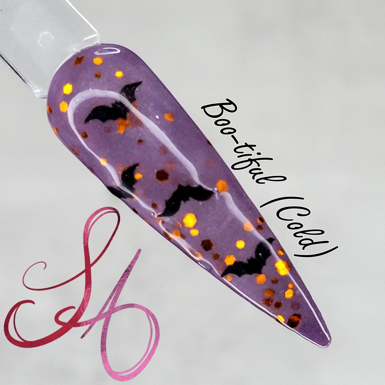 May include: A purple nail polish with a glittery finish and black bat silhouettes. The text "Boo-tiful (Cold)" is written on the right side of the image.