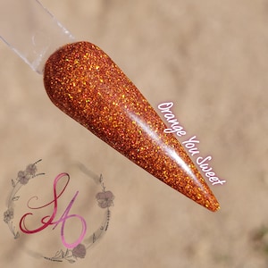 May include: A nail swatch coated in orange glitter. The text "Orange You Sweet" is written on the side of the swatch. The swatch is held by a clear plastic stick. A floral logo is in the bottom left corner.