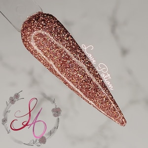Puede incluir: Primer plano de un esmalte de uñas de purpurina de color oro rosa con un diseño de línea blanca. El texto "Love Potion" está escrito en la uña.