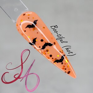 May include: A peach-coloured nail polish with black bat silhouettes and gold glitter. The text "Boo-tiful (hot)" is written on the side of the nail.