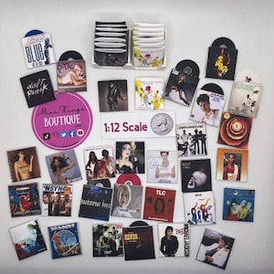 May include: A collection of miniature 1:12 scale vinyl records featuring various artists and album covers, including Pink, Backstreet Boys, TLC, and No Doubt. The records are displayed on a white surface with a sign that reads "1:12 Scale".