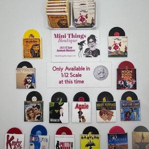 May include: A collection of miniature vinyl record covers featuring popular musicals like The Lion King, Les Miserables, Grease, Wicked, Annie, Mary Poppins, High School Musical, West Side Story, Kinky Boots, Hairspray, Pretty Woman, Beach Blanket Babylon, and Priscilla. The covers are displayed on a white background with a sign that reads "Mini Things Boutique 1:6 & 1:12 Scale Handmade Miniatures MiniThingsBoutique.com Only Available in 1:12 Scale at this time."
