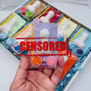Puede incluir: Un conjunto de seis figuras de cerámica blanca con botes de pintura y pinceles. Las figuras están en una caja con papel picado azul y blanco. Los botes de pintura son de varios colores, incluyendo azul, naranja, rosa y verde.