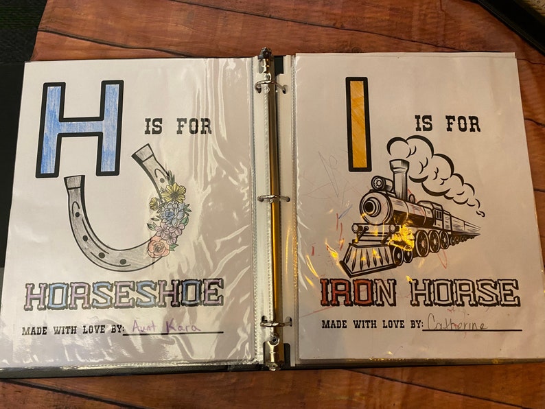 May include: A two-page spread from a children's alphabet book. The left page features the letter H in blue with a horseshoe illustration and the text "H is for Horseshoe". The right page features the letter I in yellow with an illustration of a train and the text "I is for Iron Horse".