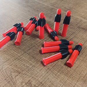 Puede incluir: Un grupo de dardos rojos y negros con puntas negras. Los dardos est&aacute;n dispuestos en semic&iacute;rculo sobre una superficie de madera.