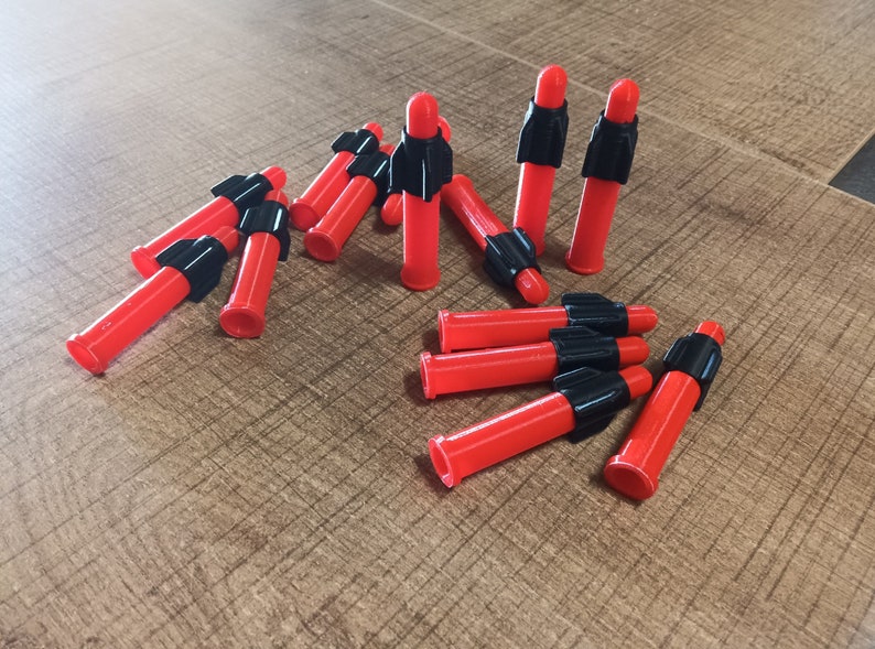 Puede incluir: Un grupo de dardos rojos y negros con puntas negras. Los dardos est&aacute;n dispuestos en semic&iacute;rculo sobre una superficie de madera.