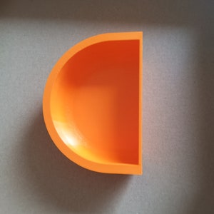 May include: A bright orange half-circle shaped dish made of ceramic. The dish is empty and has a smooth, glossy finish.