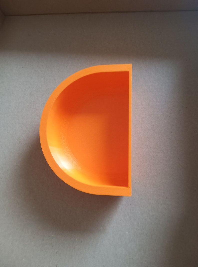 May include: A bright orange half-circle shaped dish made of ceramic. The dish is empty and has a smooth, glossy finish.