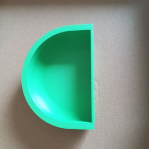 May include: A green half-circle shaped planter or dish. The planter is made of a smooth, solid material.