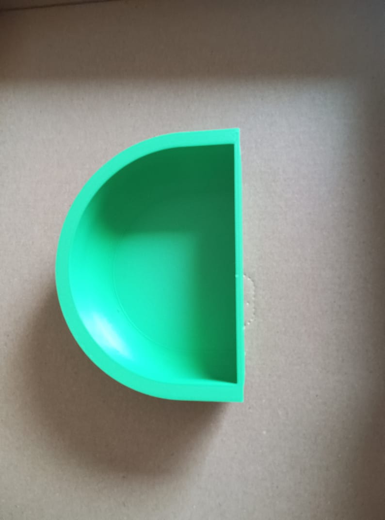 May include: A green half-circle shaped planter or dish. The planter is made of a smooth, solid material.