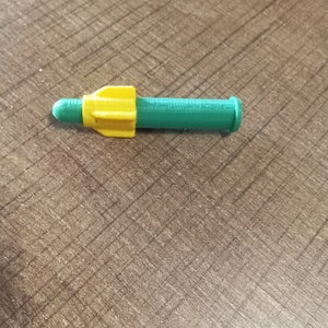 Puede incluir: Un misil de juguete de pl&aacute;stico verde y amarillo con una punta puntiaguda y una parte posterior redondeada.